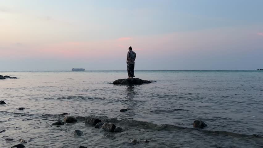 Silhouette of a man standing on a rock in the ocean during sunset at Koh Larn, Pattaya.