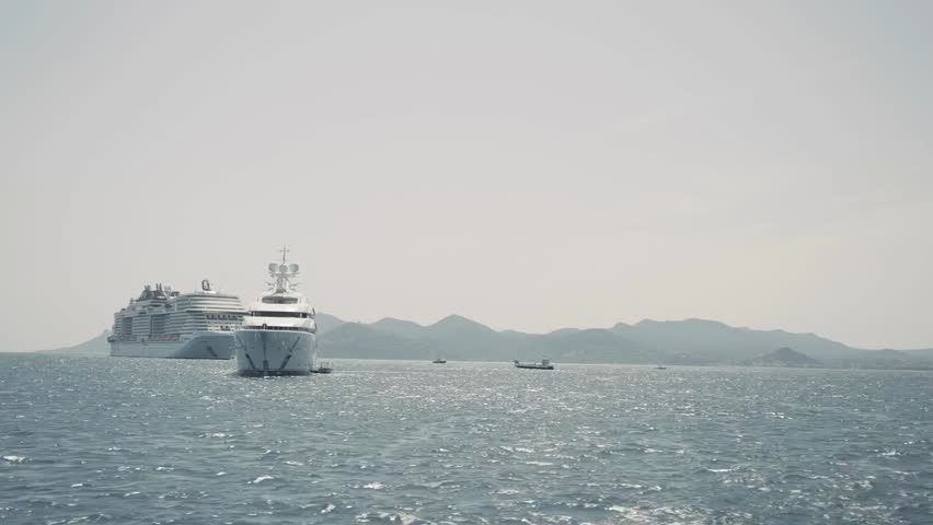 Aerial view of a luxury yacht cruising at sea alongside a cruise ship, rippling water highlighting motion and elegance.