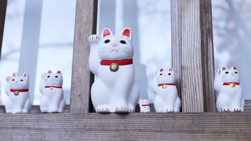 Small Maneki-neko cats sitting on wooden ledge.