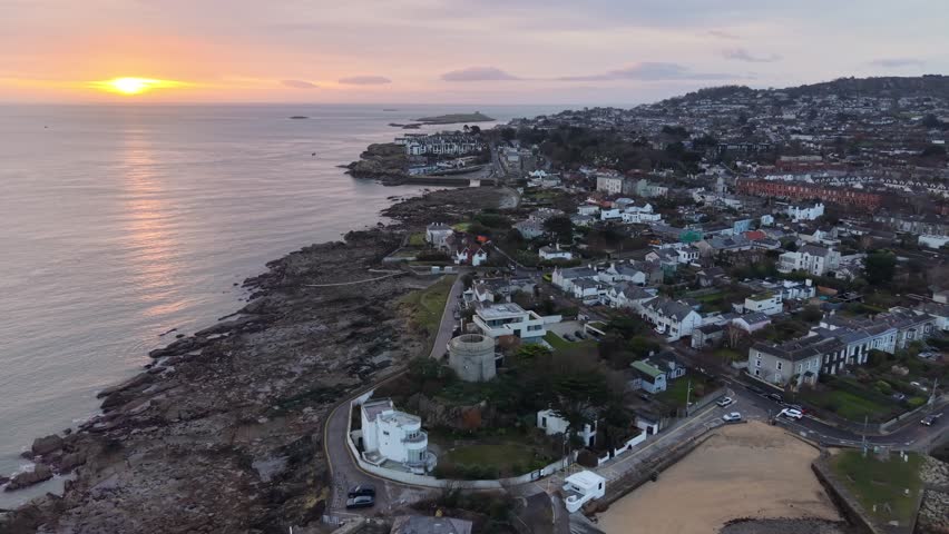 Cinematic drone orbit of Sandycove Point at sunrise, overlooking Dublin Bay on Ireland’s east coast. The shot circles the historic James Joyce Tower and Museum (Joyce’s Tower), capturing the calm morning light as it rises behind Dalkey Island and the coastline stretching toward Dún Laoghaire.
The footage highlights the Martello tower made famous as the opening setting of Ulysses by James Joyce, along with the Forty Foot bathing place and the rugged granite shoreline of Sandycove.
Location: Sandycove, County Dublin, Ireland
Shot type: Drone aerial orbit
Time of day: Sunrise, Early morning
Style: Cinematic, natural light, coastal landscape