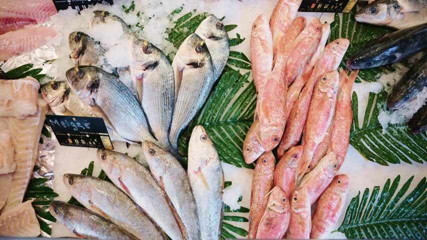 Fresh seafood display with a variety of fish including red mullet and seabream on ice with green garnishes for sale at a fish market