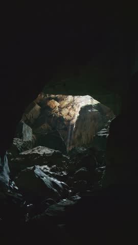 Sunbeam shines through an opening into dark mysterious cave in Laos creating an ethereal light ray on the rocks on Southeast Asia
