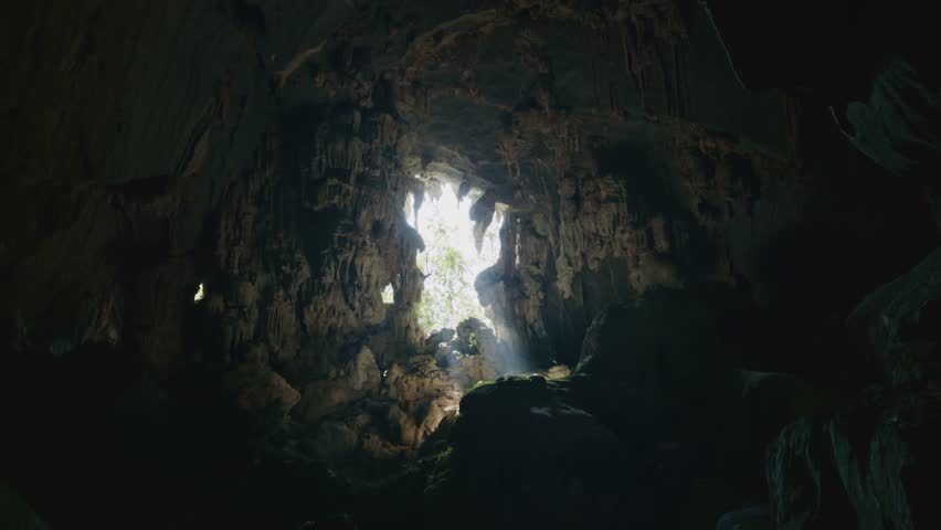 Eerie sunlight shines inside large natural cave in Laos, Southeast Asia, illuminating subterranean interior and rock walls