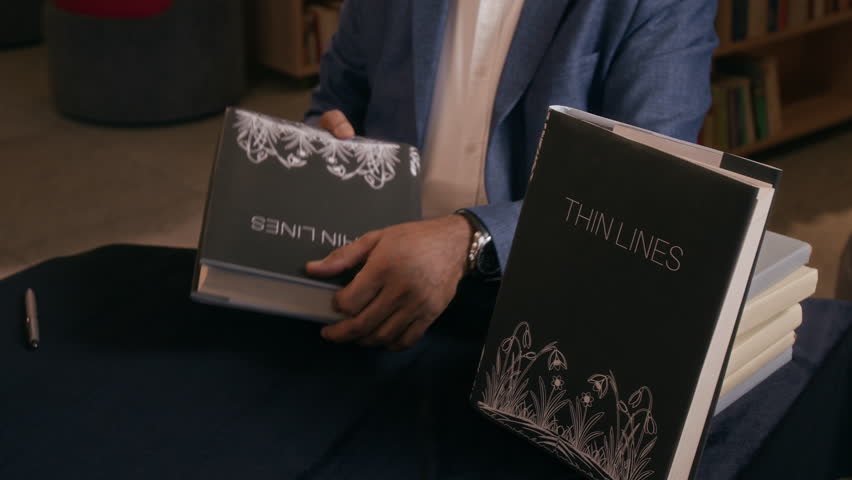 High angle shot of unrecognizable man in formal outfit selling copies of his books while sitting at table in book store