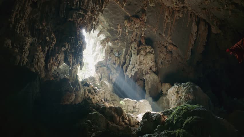 Sunbeam illuminates a dark mysterious cave with stalactites and stalagmites in Laos, Southeast Asia, alternative destination for backpackers