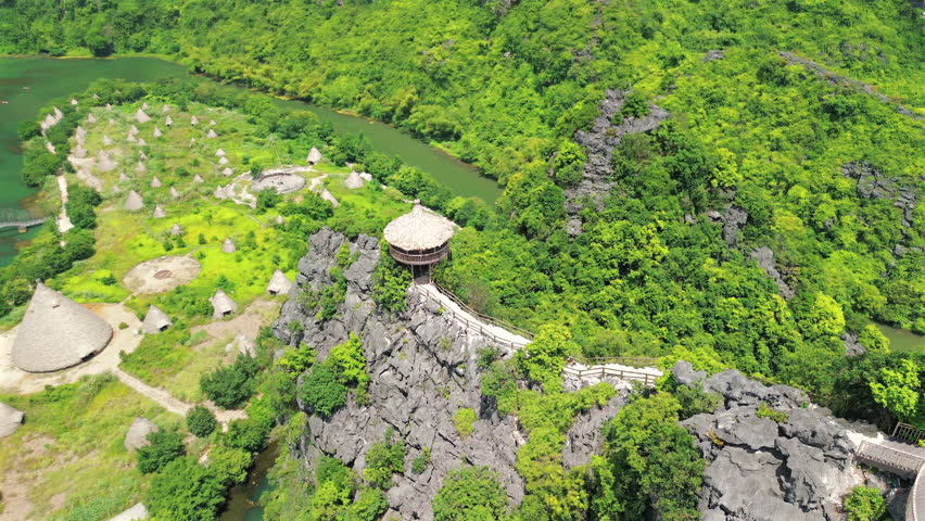 A breathtaking drone shot showing the Kong Island and a wooden pavilion perched on a steep limestone cliff overlooking a turquoise river in Vietnam.