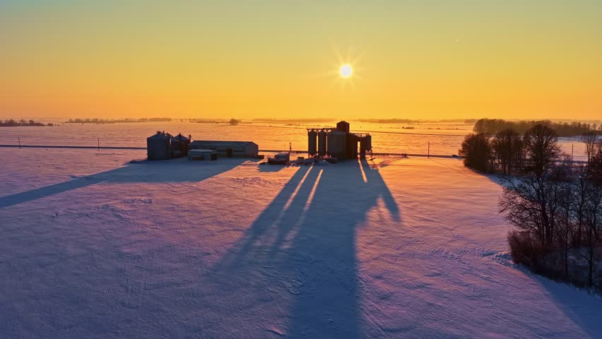 Sunrise Over A Snowy Farm With Grain Silos And Farm Elevator In Winter. - aerial shot