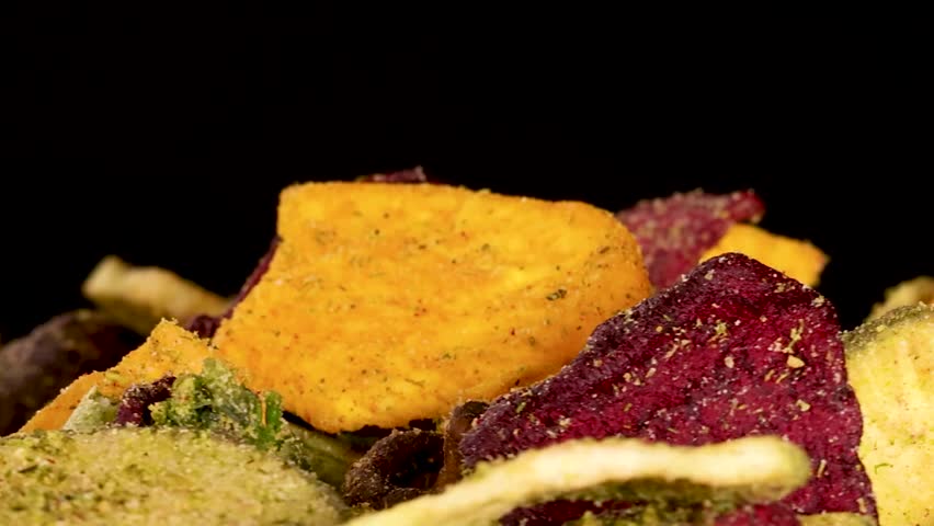 A close-up shot of fingers selecting colorful dried vegetable chips from a pile.