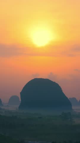 Cinematic sunrise footage of the limestone hills of Din Daeng Doi in Krabi, Thailand, as the camera pans slowly sideways across a glowing orange sky and misty tropical landscape. Travel concept.