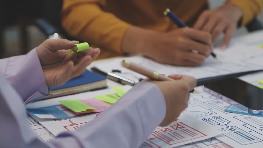 Team of uxui designers pointing at computer screen, discussing new mobile app design in the office
