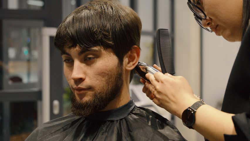 Barber shaping sideburns of a man with electric shaver
