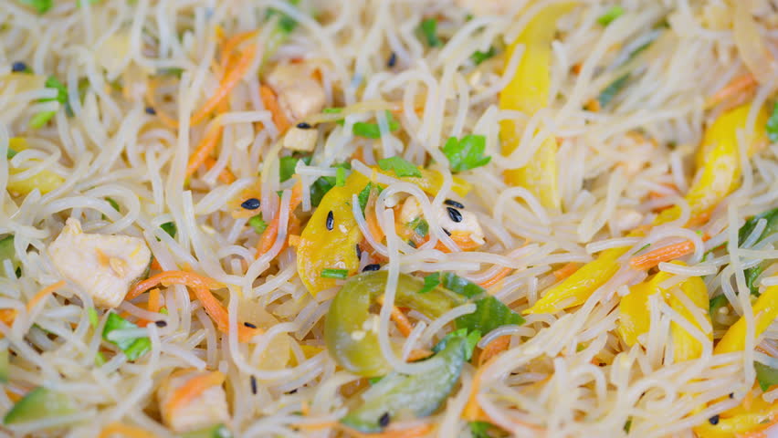 closeup rice vermicelli noodles stir fry with colorful julienned carrot and yellow pepper, chopped cilantro, toasted sesame seeds and glossy oil sheen, soft