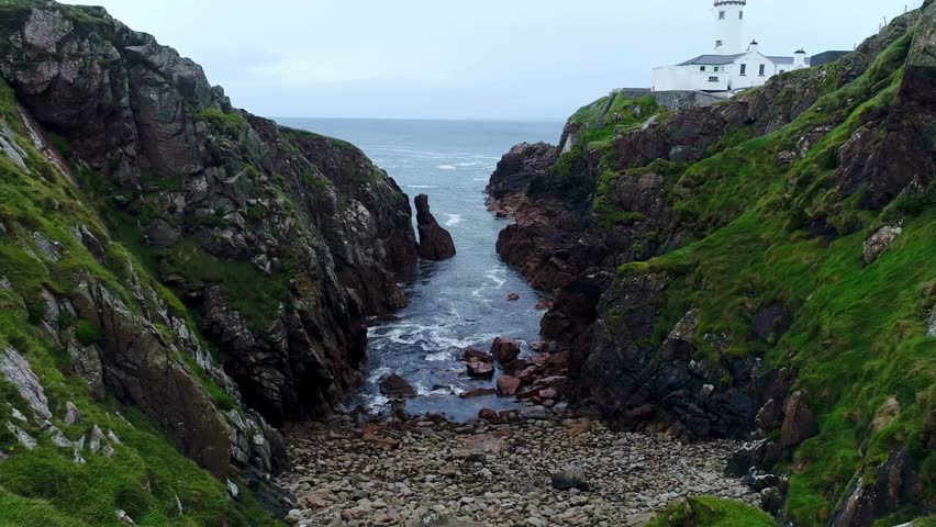 Stunning landscape showing a lighthouse positioned on rocky cliffs near the ocean, waves crashing against stones in a remote coastal area, highlighting nature