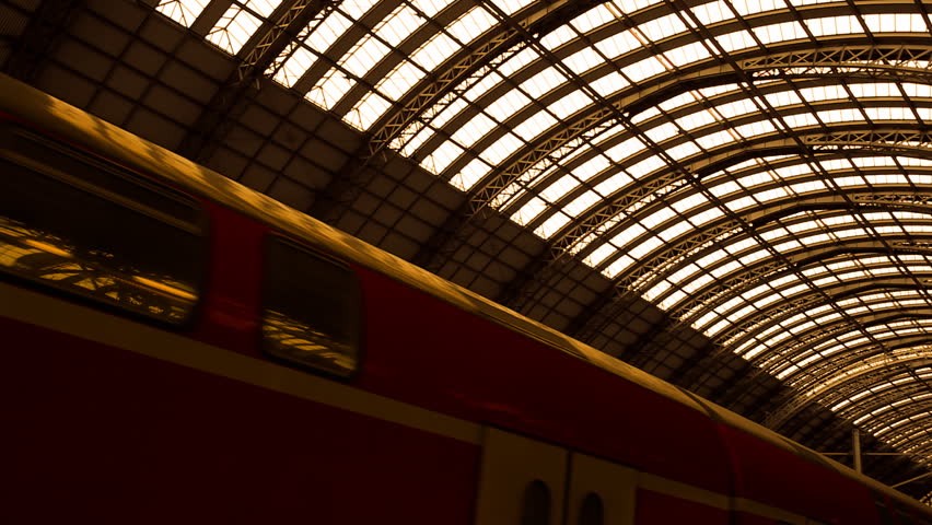 Red train accelerates under an old looking architectural structure from steel