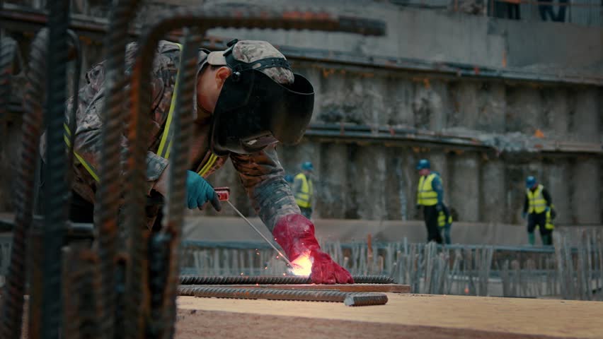A worker at a construction site welds metal with a welding machine