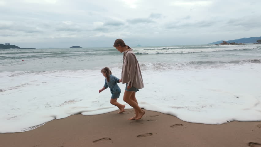 Child and adult play in the ocean waves at the beach during a cloudy day