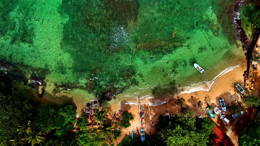 Aerial view of turquoise waters and rocky shoreline at Dondra Head, highlighting lush green coastline and seaside path.