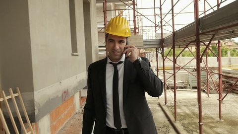 Profession, business and telecommunications, architect talking on cell phone and walking in construction site under building scaffolding. Steadicam shot