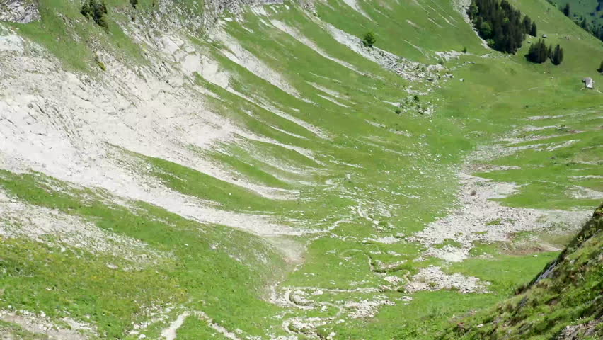 A sweeping view of a lush green hillside featuring rocky cliffs and a serene landscape. The scene captures the beauty of nature in a tranquil setting.