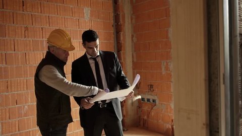 Apartment plumbing system and professional jobs, plumber and engineer talking and looking at building plans in construction site. Steadicam shot