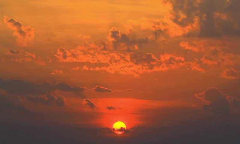 Golden sunset over horizon with dramatic orange sky and glowing sun above clouds