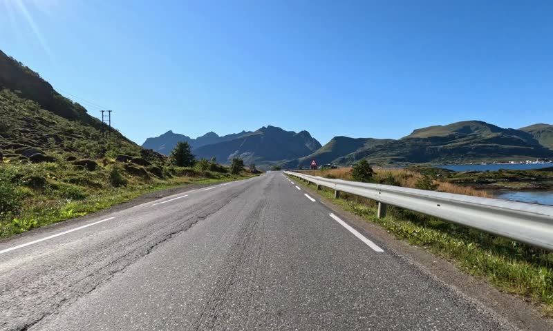 Car driving on scenic mountain road under clear blue sky with bright sunlight and landscape