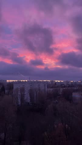 Red cloudy sky over a big city at sunset. View from above, below you can see residential areas with high-rise buildings and a boiler room chimney from which smoke is emitted. Panorama.