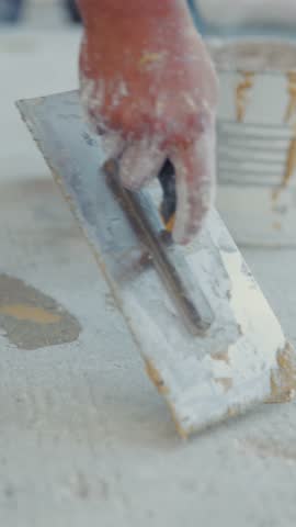 Close-up of a worker's hand applying plaster to a concrete surface with a putty knife