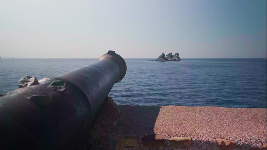 Panoramic view of historic iron cannon on Petrovac waterfront pointing to sea with calm blue waters in background