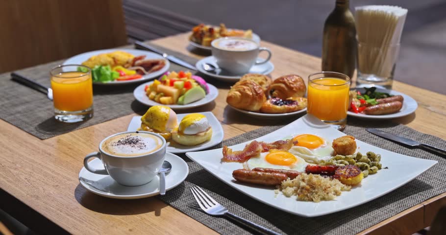 Assorted breakfast dishes sitting on wooden table in sunny cafe, fried eggs, bacon, pastries, fresh fruit and coffee, bright morning light, luxury hotel dining, brunch lifestyle.