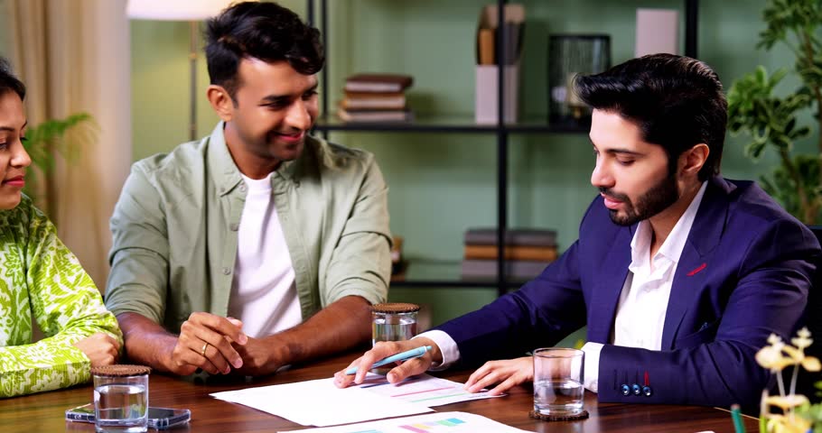 Indian couple meeting shaking hands with financial planner or ca in his office with laptop after reviewing growth reports and projections during serious investment discussion across table in office