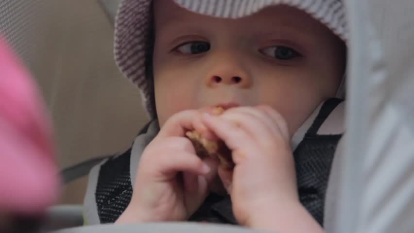 A baby eating a peanut butter sandwich in his carrier while on a hike