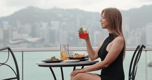 Woman in black dress sitting at rooftop restaurant holding red cocktail, Hong Kong skyline. Luxury travel, urban lifestyle, fine dining, city vacation, summer holiday, tourism, leisure. - Powered by Shutterstock - Get 15% off with code: PIKWIZARD15