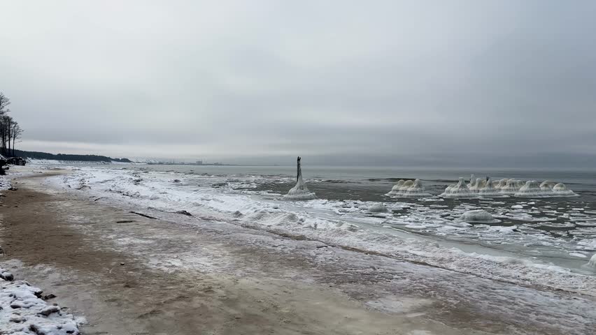 Winter seascape of the Baltic Sea with thick ice formations and snow along the shoreline under a cloudy gray sky.