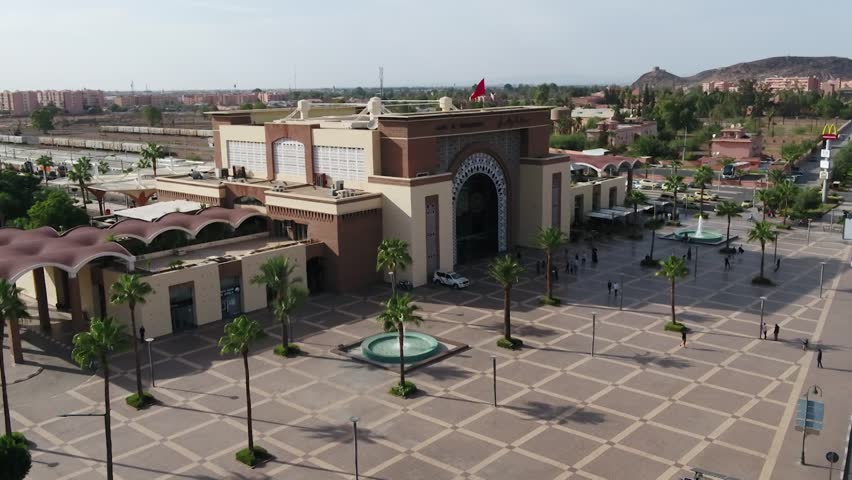 Detailed drone shot of the Marrakech Railway Station facade. Highlights the stunning blend of Islamic arches and modern design, featuring the grand plaza, fountains, and surrounding city.