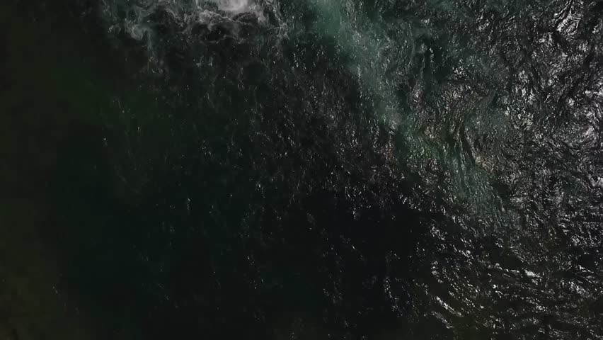 Drone footage captured from above showing a waterfall plunging into calm water, highlighting the dynamic flow, foam, and natural beauty of the cascading water.
