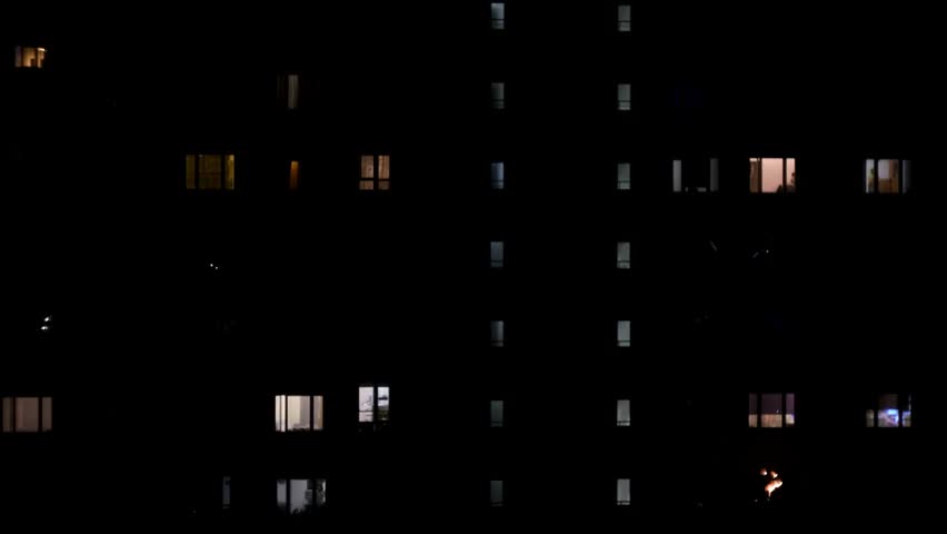 Night view of illuminated windows in a multistorey building, capturing urban life, residential apartments, and city lights in the evening.