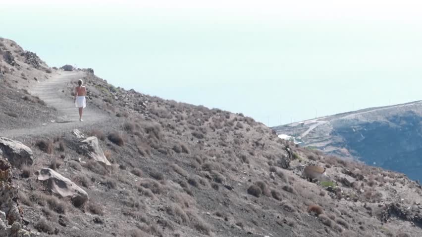 Woman walking from Oia to Fira through the rock volcanic sand path with Aegean Sea view in Santorini during summer. Santorini hiking.