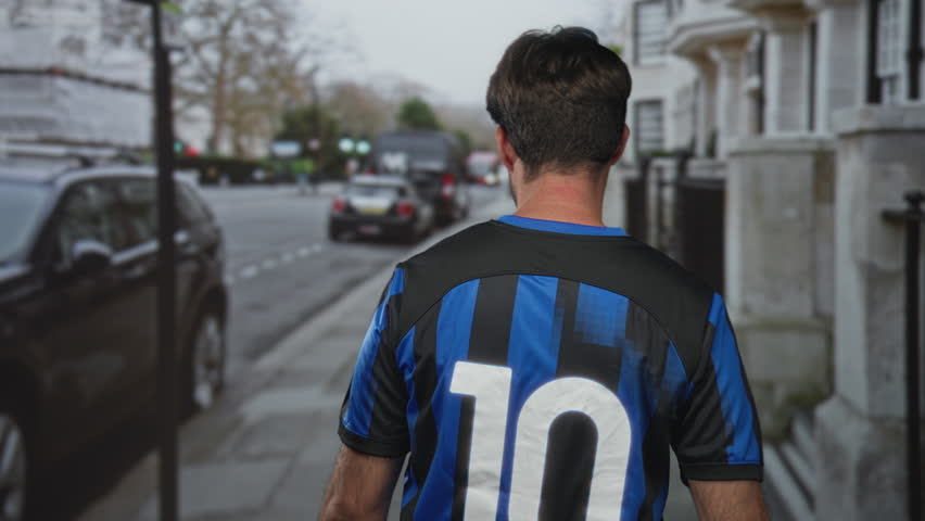 Man in blue and black number 10 soccer jersey walking down a city street with back to camera and parked cars nearby; team pride.