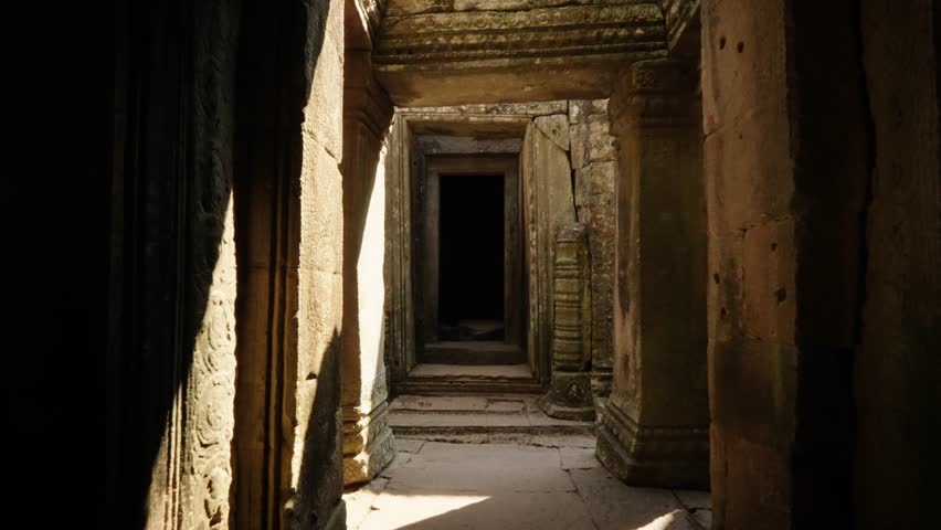 Sunlit stone corridor leading to a dark inner doorway at Angkor Wat in Cambodia