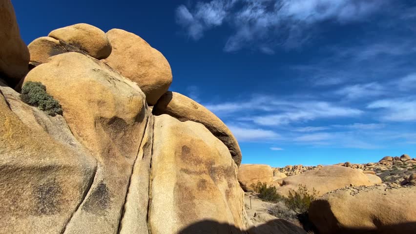 🏜️ Desert Wonders: Scenic Rock Formations in Joshua Tree. Smooth cinematic reveal of unique rounded rock formations and boulders in Joshua Tree National Park. Desert vegetation under a bright sun and blue sky. Atmosphere of unforgettable adventure.