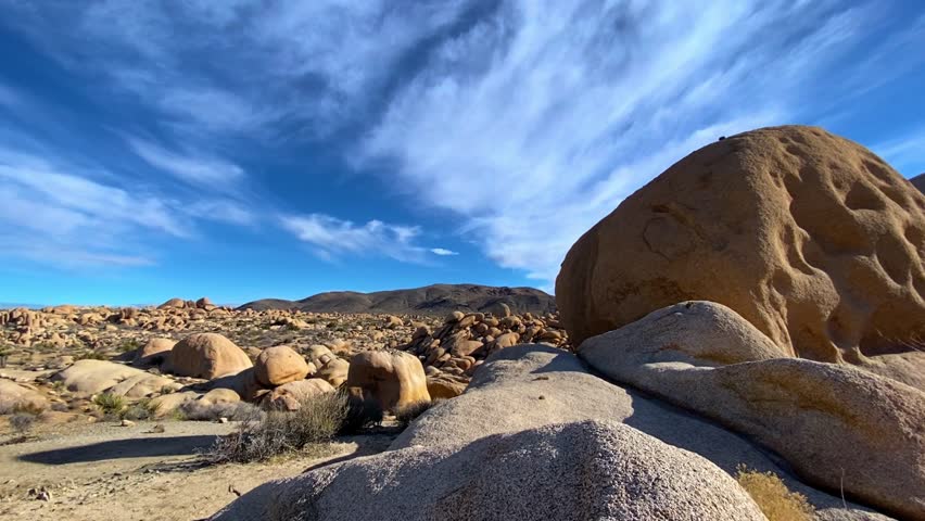 🏜️ Desert Wonders: Scenic Rock Formations in Joshua Tree. Smooth cinematic reveal of unique rounded rock formations and boulders in Joshua Tree National Park. Desert vegetation under a bright sun and blue sky. Atmosphere of unforgettable adventure.