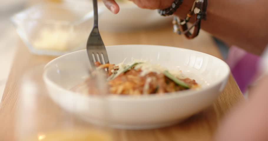 Fork entering frame is puncturing spaghetti in bowl on table, twisting strands and lifting for bite. Cuisine, culinary, food photography, gourmet, dining, presentation, rustic