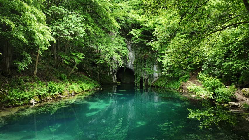 Emerald waters of Krupajsko Vrelo spring surrounded by lush green forest in Serbia. Crystal clear natural source with cave entrance and tranquil reflection