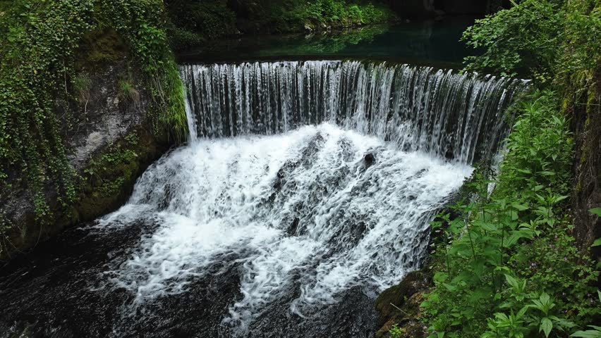 Small waterfall in lush green forest with clear freshwater flowing over rocks. Natural cascade surrounded by vegetation in peaceful Serbian landscape