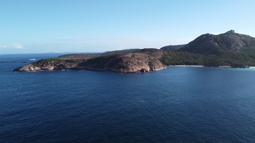 Wide aerial drone shot capturing the perfectly curved shoreline of Hellfire Bay in Cape Le Grand National Park, Western Australia. Crystal clear turquoise water and pristine white sand surrounded by granite formations create an iconic Australian coastal landscape.