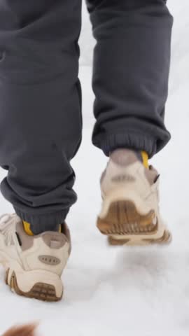 Person walking away in snow, turning back to pet small dog on narrow path, reinforcing emotional connection.