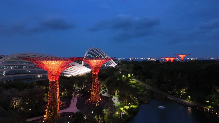 Singapore by Night – 4K aerial drone footage of marina bay sands, city skyline, skyscrapers, luxury hotels, gardens by the bay, garden Rhapsody, dome and river illuminated in financial district. 