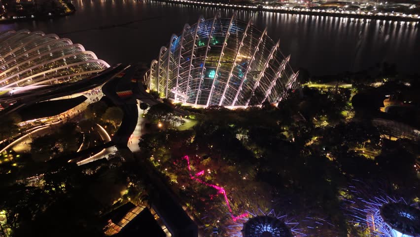 Singapore by Night – 4K aerial drone footage of marina bay sands, city skyline, skyscrapers, gardens by the bay, garden Rhapsody, dome and river illuminated in financial district.