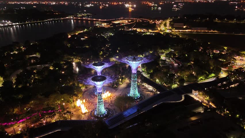 Singapore by Night – 4K aerial drone footage of marina bay sands, city skyline, skyscrapers, gardens by the bay, garden Rhapsody, dome and river illuminated in financial district.